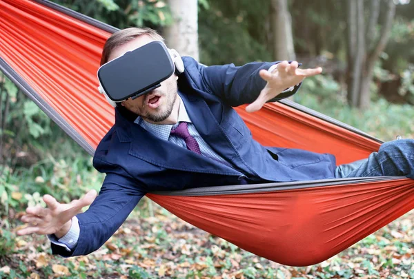 Surprised businessman uses vr glasses, resting in a hammock. Virtual reality or future technology concept.