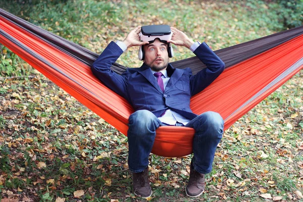 Very surprised businessman after using vr glasses. He resting in a hammock on nature. Virtual reality or future technology concept.