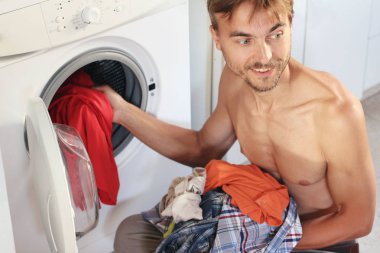 Yakışıklı genç çamaşırları çamaşır makinesi yükler. Erkek ev kadını kavramı.