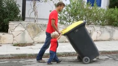 Baba ve oğul birlikte itme büyük sokakta tekerlekli çöp kutusu. Ekoloji veya aile ekip çalışması kavramı. 