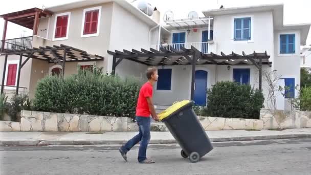 カジュアルな服を運ぶ大きなゴミで若い男が過去のカラフルな家 プロタラス キプロスの車輪の上 — ストック動画