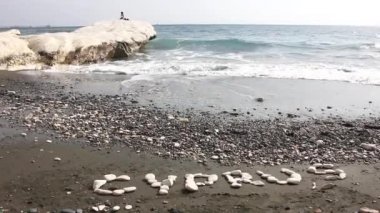 Siyah kum ve beyaz kayalar ile ünlü Vali plaj. Yazıt Kıbrıs'tan su kenarındaki taş.
