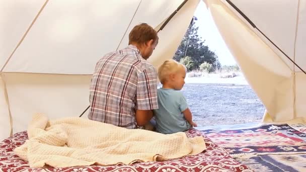 家庭的魅力 父亲和他的幼儿儿子在舒适的内部的大野营帐篷内使用智能手机 豪华旅行适应入森林 — 图库视频影像