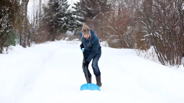 カジュアルウェア雪を投げ入れる 雪に覆われた道路の雪かきとギターのようなシャベルで再生を開始で変な男 冬の楽しみの概念 — ストック動画