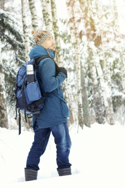 Yakışıklı sakallı uzun yürüyüşe çıkan kimse adam sırt çantası ve termos sıcak giysiler içinde karlı kış ormanda yola. Sezon kavramı. 