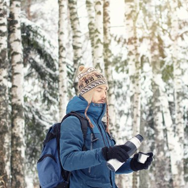 Yakışıklı uzun yürüyüşe çıkan kimse adam sıcak giysiler içinde çay kupa termos içinde kış orman üzerinden dökülen. Sezon kavramı. Kare. 