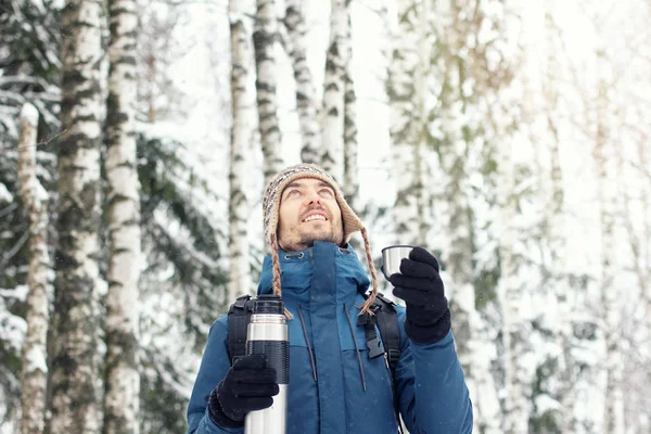 魔法瓶と暖かい服装でハンサムなハイカー人類旅行冬の森の雪の日 彼は見上げるし 笑顔します シーズン コンセプト コピー スペース — ストック写真