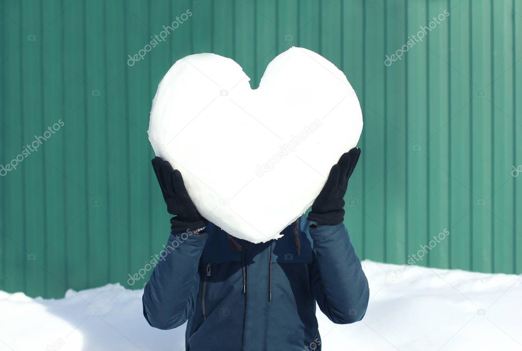 Man in winter clothes with big heart made of snow instead his he