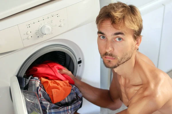 Un joven guapo carga la ropa en la lavadora. M — Foto de Stock