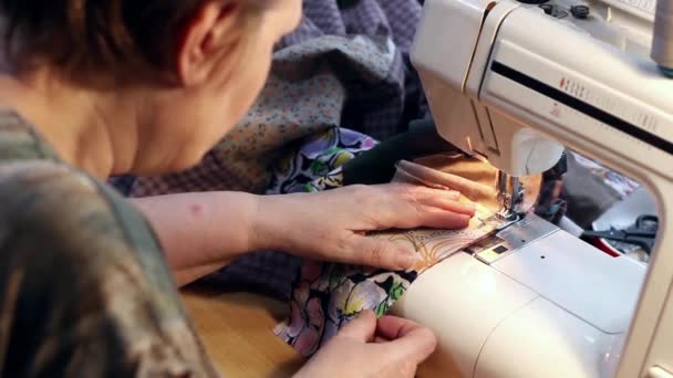 Zralá žena šije patchwork deka na šicí stroj, zaměření na nohy stroje. Pravé boční pohled.