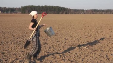 Gün batımında taze sürülmüş alanda zor bir gün sonra kürek ve kova dansları ile Mutlu komik kadın çiftçi.