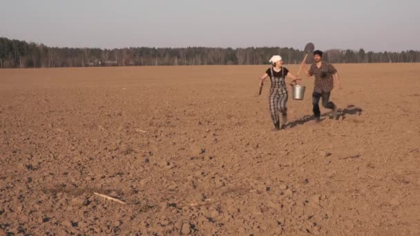 两个滑稽的农民男人和女人在刚犁地里跑来跑去 携带铲子 铲叉和铲斗 播种季节概念 — 图库视频影像
