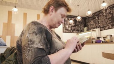 Kafede otururken ve kahve beklerken cep telefonu kullanan çekici olgun beyaz kadın.