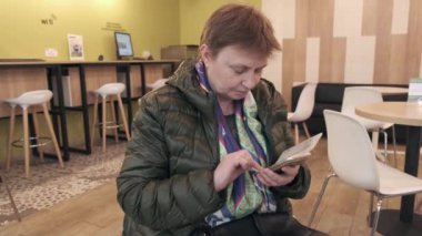 Kahve dükkanında beklerken akıllı telefon kullanan gündelik giyim yakışıklı yaşlı kadın. 