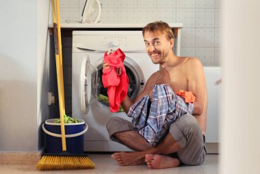 Mutlu yakışıklı gülümseyen adam çamaşırları çamaşır makinesine yükler. Bekar ev işleri, erkek ev hanımı kavramı. 