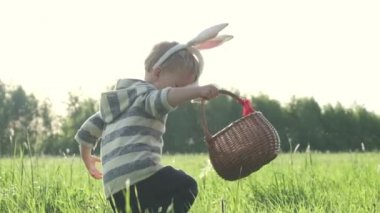 Paskalya günü bahar bahçesinde veya çayırpaskalya yumurtası için avcılık sevimli tavşan kulakları ile sevimli çocuk, geleneksel kutlama. Paskalya ziyafeti konsepti. Yavaş çekim. 