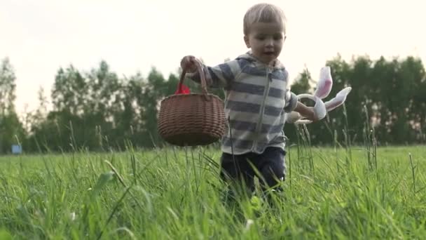 イースターエッグハント かわいい面白いブロンドの子供は 緑の草原で実行され 見つけて ウィッカーバスケットにカラフルな卵を収集します スローモーション クローズ アップ — ストック動画