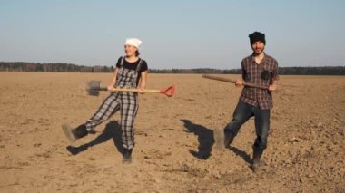 İki komik çiftçi adam ve kadın kürek ve pitchfork dansları taze sürülmüş alanda. Mutlu tarım konsepti.