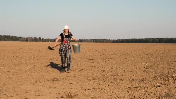 有趣的快乐女农民跑过犁地 跳向一边铲和桶 慢动作 — 图库视频影像