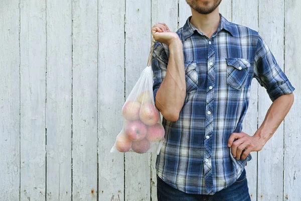 Zéro déchet et concept de mode de vie écologique. Homme tenant sac à provisions réutilisable avec des pommes sur fond mural en bois . — Photo