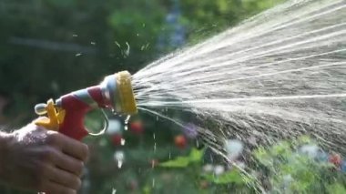 Yavaş çekim. Bahçedeyken elinde su hortumu fıskiyesi tutan bir adam. Fıskiyeden fışkıran su püskürtme.