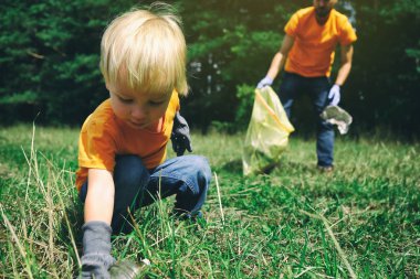 Gönüllüler parkta çöp topluyorlar. Baba ve küçük oğlu ormanı temizliyor. Küçük çocuk kirliliği çevreyi kurtarmak için doğa üzerinde plastik çöp toplar.