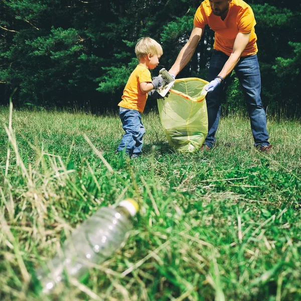 Önkéntesek felszedését alom a parkban. Apja és kisgyermek fia megtisztítása erdőben. Kisfiú gyűjt műanyag szemetet a természetben, hogy mentse környezet szennyezés. Square. — Stock Fotó