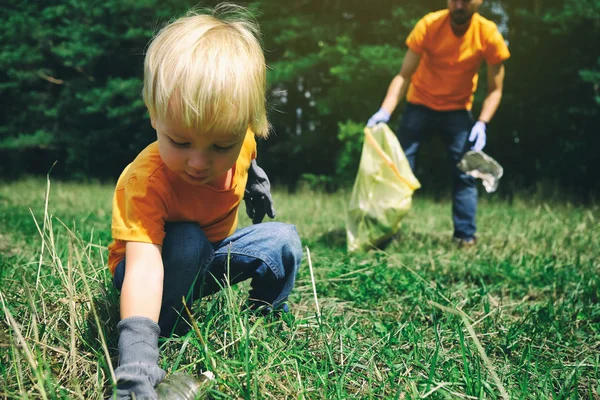 Des bénévoles ramassent des déchets dans le parc. Père et son fils tout-petit nettoient la forêt. Petit garçon recueille des déchets plastiques sur la nature pour sauver l'environnement de la pollution . — Photo