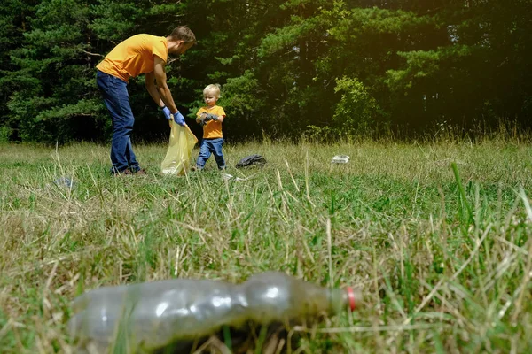 Father and his little son collecting garbage and plastic bottles in the park. Volunteers family picking up litter in the forest. Environmental protection concept. Copy space. — Stock Photo, Image