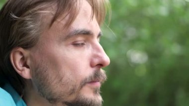 Yeşil gözlü yakışıklı sakallı beyaz adam kameraya döner ve gülümser. Yavaş çekim. Bulanık doğa arka planı.