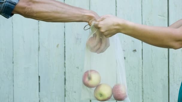 女人的手拿着可重复使用的再生网制作袋 男人的手把苹果放在木质背景上 — 图库视频影像