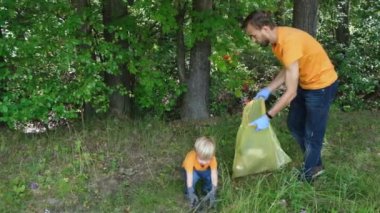 Gönüllüler parkta çöp topluyorlar. Baba ve küçük oğlu ormanı temizliyor. Ebeveynleri ile küçük çocuk kirlilikten çevreyi kurtarmak için doğa üzerinde plastik çöp toplar.