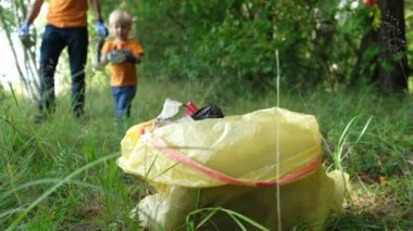 Baba ve oğul gönüllüleri çevreyi kirlilikten kurtarmak için doğaüzerinde plastik çöp toplar. Çöp torbası ön planda.