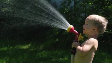 Moskova, Rusya - 14 Haziran 2019: Sevimli bebek sarışın çocuk ve babası arka bahçesinde bahçe fıskiye ile oynuyor. Aile yaz sıcak gün zevk. Küçük çocuk hortumdan gelen suyla babasını doldurur. Mutlu çocukluk. Yavaş çekim.