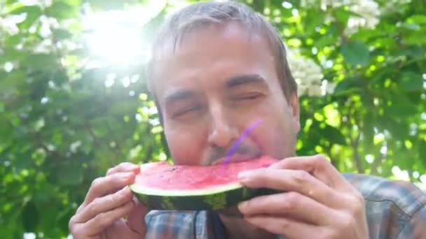 面白い大人のひげの男は レンズフレアで緑の自然の背景にスイカを食べます 夏の食べ物コンセプト — ストック動画