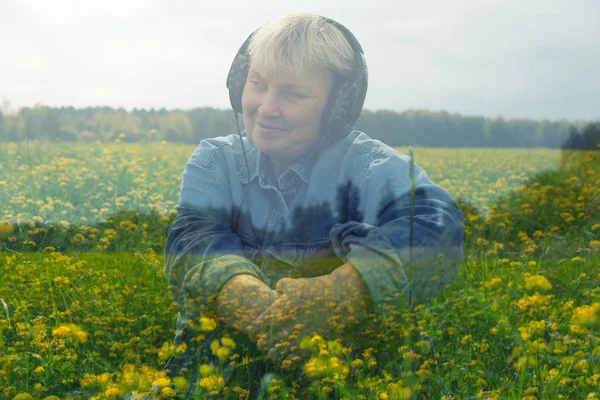 Šťastná usměvavá žena, která sedí na sluchátkách a naslouchá relaxační hudbě na poli se spoustou žlutých květin. Dvojitá expozice. Zvuková terapie. Citlivost k přírodě. — Stock fotografie