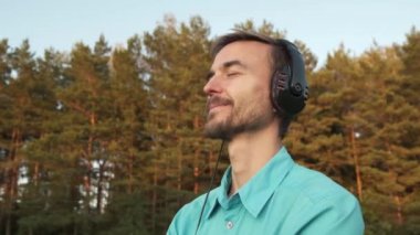 Yakışıklı genç sakallı bin yıllık adam kulaklık giydi gün batımında doğa müzik dinler. Sonik Terapi. Meditasyon. Sakin ol..