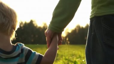 Gün batımında el ele tutuşan baba ve oğulu kapatın. Güneş ışınları arka plan ile el ele. Mutlu aile, sevgi, birliktelik.