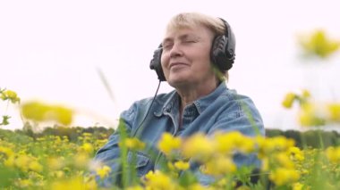 Kulaklık takan olgun kısa saçlı kadının portresini kapatın ve doğayla ilgili müzik dinleyin. alm aşağı ve meditasyon. Yavaş çekim.