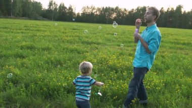 Baba ve oğul gün batımında sahada toplanmaya oynuyorlar. Babam sabun kabarcıkları üfler, ve çocuk yakalar ve onları patlar. Mutlu aile anları. Yavaş Çekim.