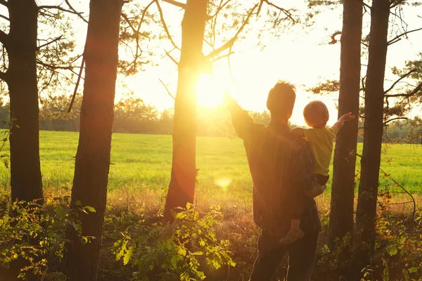 Padre sostiene a su hijo pequeño en sus brazos y abren las manos togerher para cumplir con la hermosa puesta de sol en el borde del bosque. Día del Padre, paternidad feliz, momentos familiares conmovedores . —  Fotos de Stock