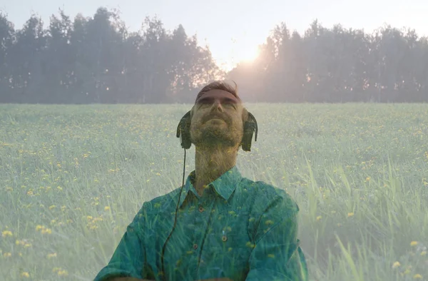 Bonito jovem barbudo vestindo fones de ouvido e ouvir música relaxante na natureza ao pôr do sol. Dupla exposição. Terapia sónica. Meditação . — Fotografia de Stock