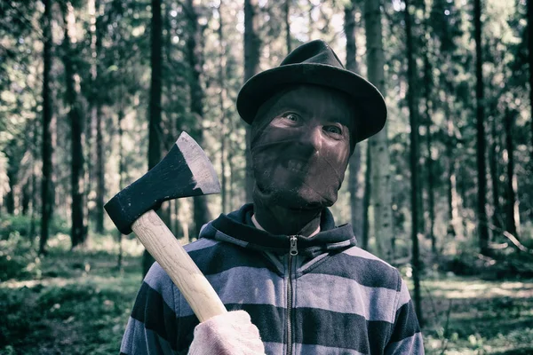 Maníaco en serie con hacha en el bosque, asesino sangriento, asesino, loco con máscara de miedo con sonrisa bestial, disfraz de halloween, concepto de horror . — Foto de Stock