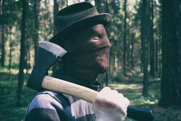 Seryjny maniak z siekierą w lesie, krwawy zabójca, morderca, szaleniec w strasznej masce i kapeluszu na świeżym powietrzu, kostium Helloween, koncepcja horroru. — Zdjęcie stockowe