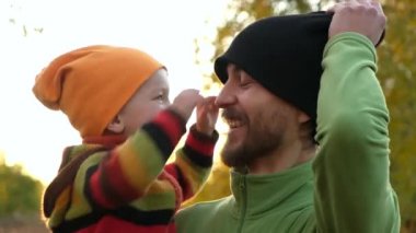 Baba ve oğul gün batımında sonbahar parkında birbirlerinin şapkalarını çekerek oynuyorlar. Sonbahar sezonunda mutlu bir aile. 