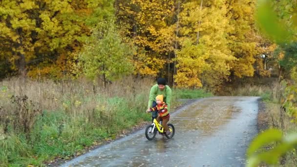 父亲在秋天的公园教他的小孩骑自行车 孩子们练习骑自行车 快乐的家庭时刻 爸爸和儿子在一起的时间 糖果生活方式镜头 — 图库视频影像