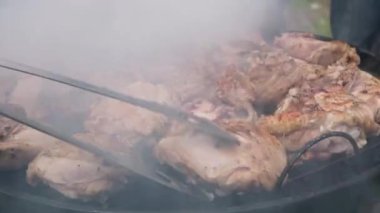 Izgarada kızartılmış et. Adam BBC 'de tavuk butlarını çeviriyor. Arka bahçede çok dumanlı barbekü..