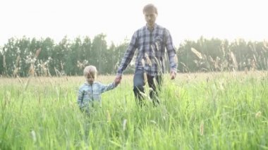 Babası ve küçük oğlu yaz tarlasında birlikte yürüyorlar, kameraya doğru ilerliyorlar. Baba ve çocuk gün batımında el ele tutuşuyorlar. Mutlu aile anları.