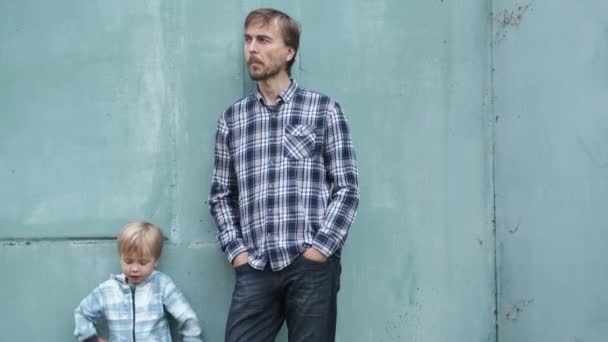 父亲节的生活方式父亲和儿子站在蓝色的墙旁边 嚼口香糖或吃东西 两代人的概念 — 图库视频影像