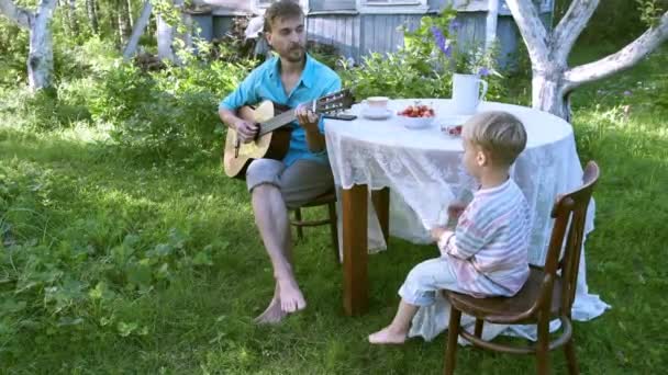 农村生活缓慢 父子俩在花园里休息 爸爸弹吉他 小孩唱歌 村里的暑假 小巧玲珑 心胸狭窄 享受小事 — 图库视频影像